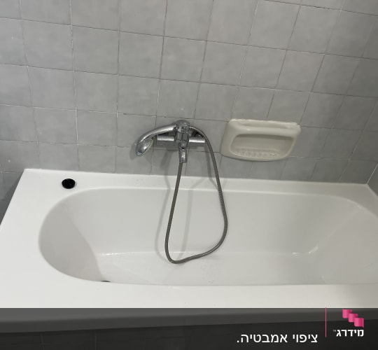 אמבטיה לבנה עם ברז ומחזיק סבון על קיר אריחים